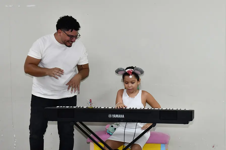Vera toca el piano mientras su papá canta rondas infantiles.